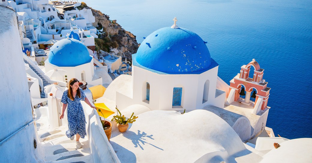 Women in a blue dress walking up the steps in Santorini, Cyclades Island